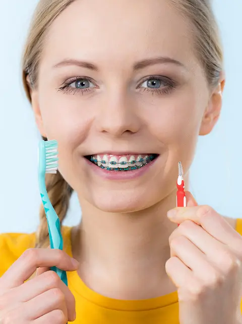 Woman with braces demonstrating brushing and flossing techniques with floss threader and toothbrush.
