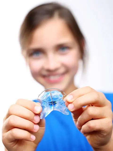 Clear orthodontic retainer in hand, care instructions for Dietrich Family Orthodontics patients.